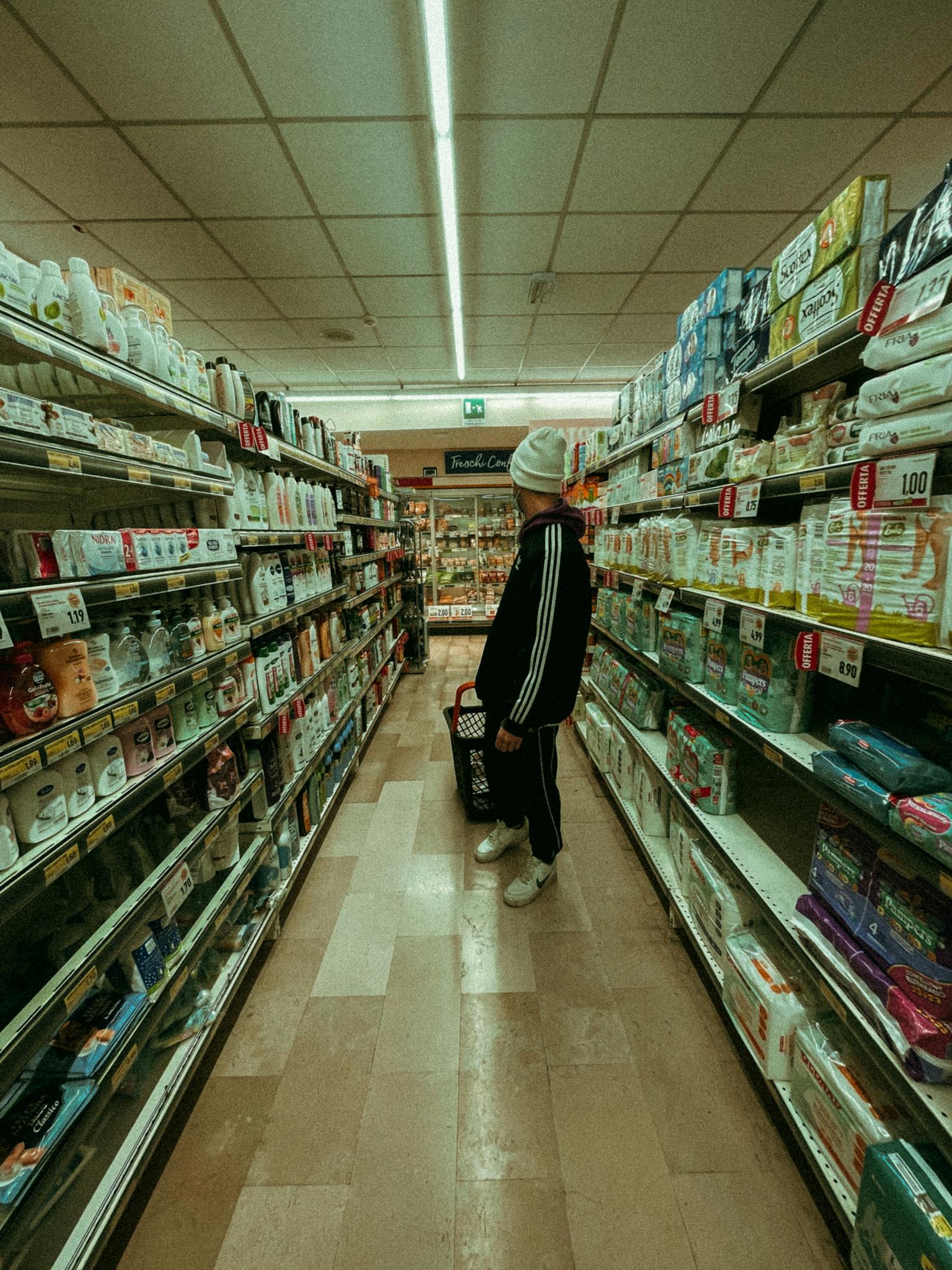 A man shop in a grocery store aisle, holding a basket with various products.
